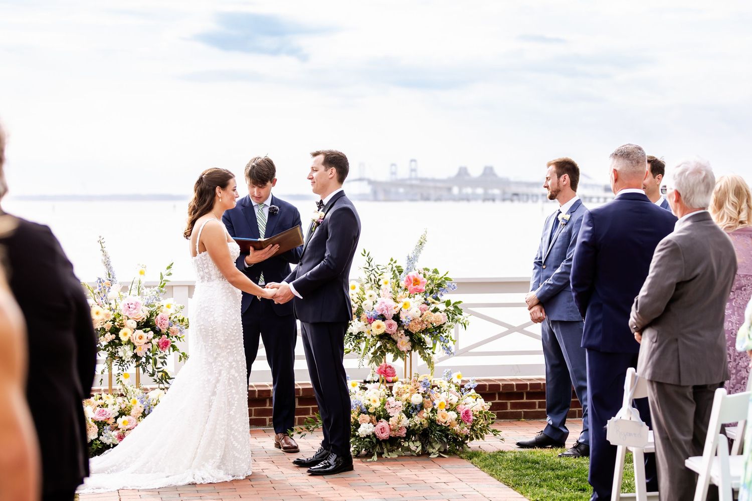 Outdoor wedding ceremony setup with guests gathered by the waterfront.