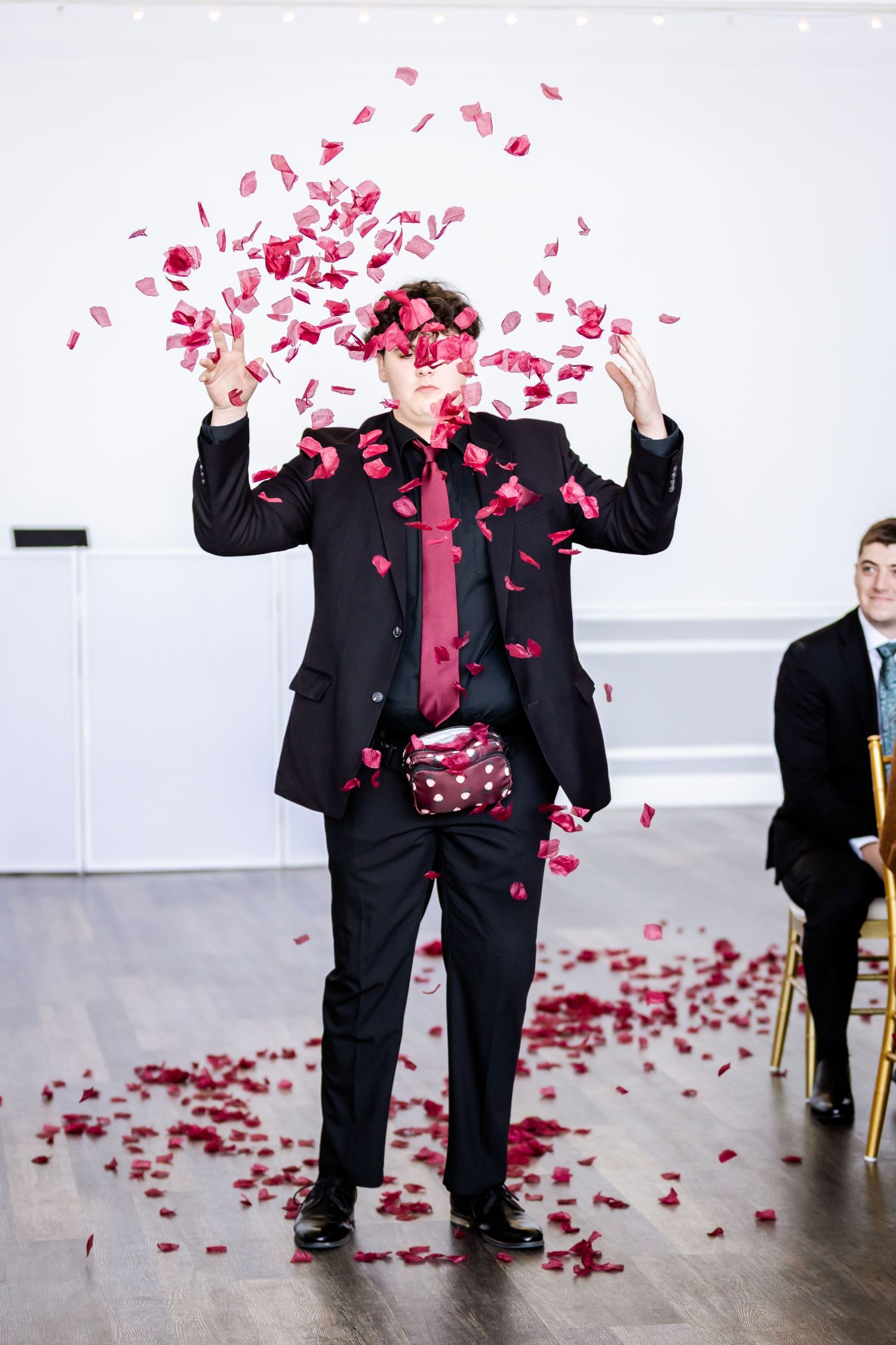 Wedding guests toss red rose petals during an indoor celebration.