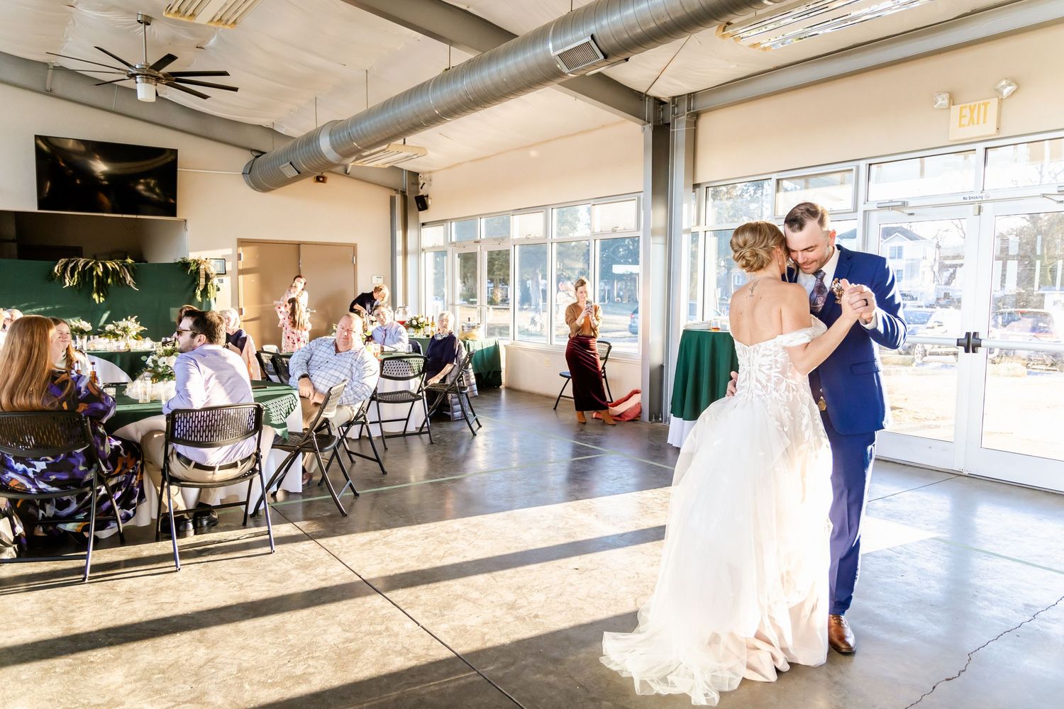 Couple sharing their first dance in an industrial-style wedding venue with guests looking on.