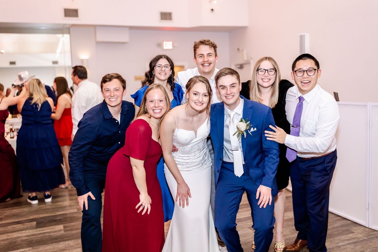 Group of wedding guests posing together for photos in a bright white reception venue.
