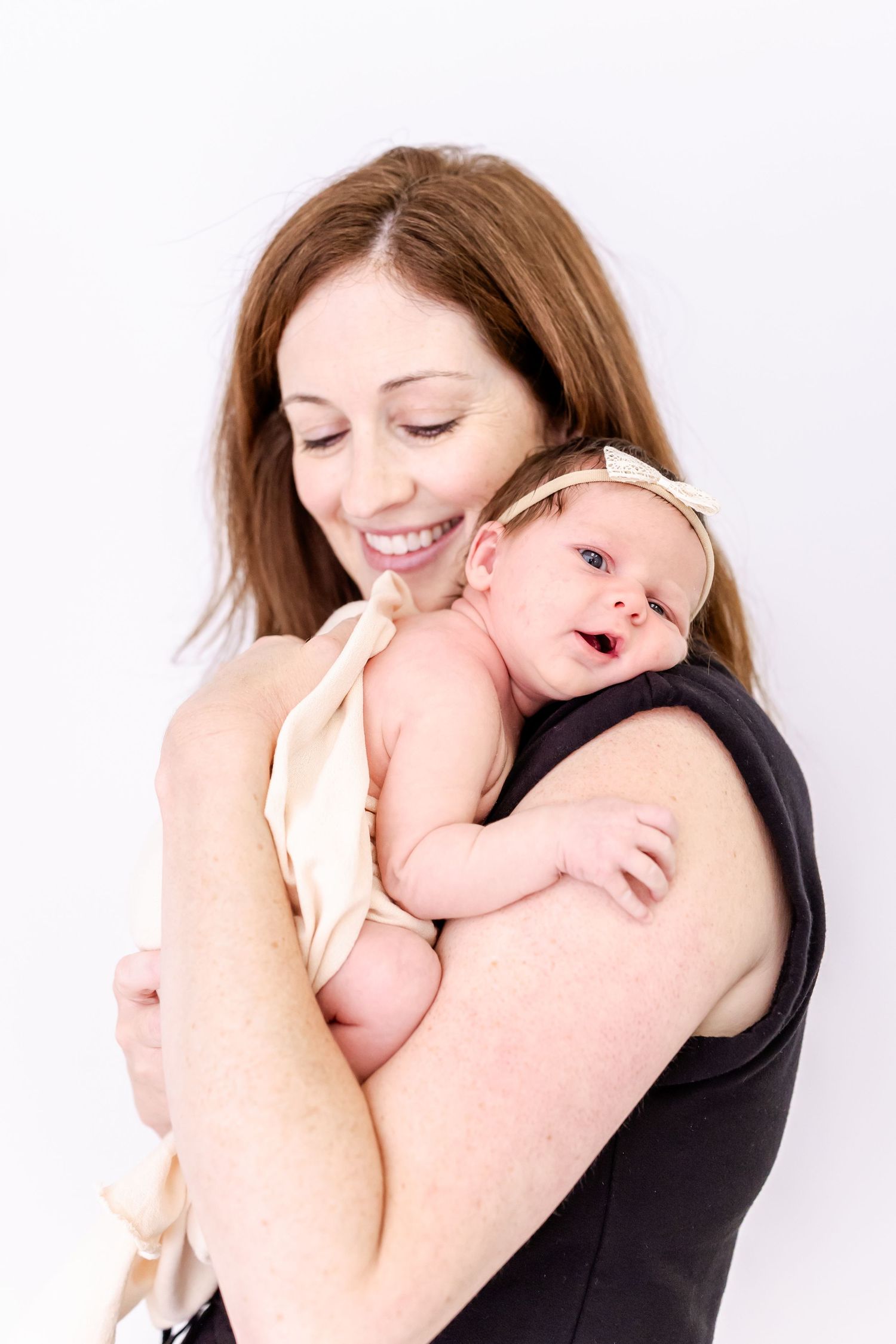Mother cradles and snuggles with her baby in loving embrace against white backdrop during professional photo session.