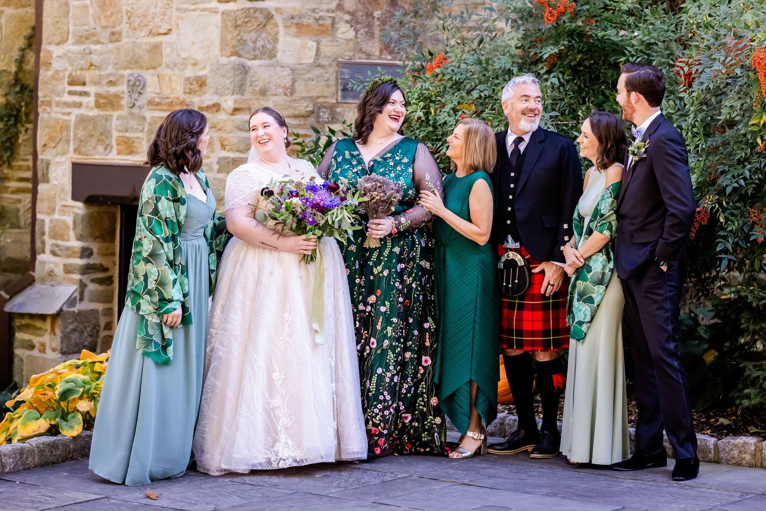 Wedding party in colorful attire gathers outdoors with emerald green dresses and vibrant floral bouquets.