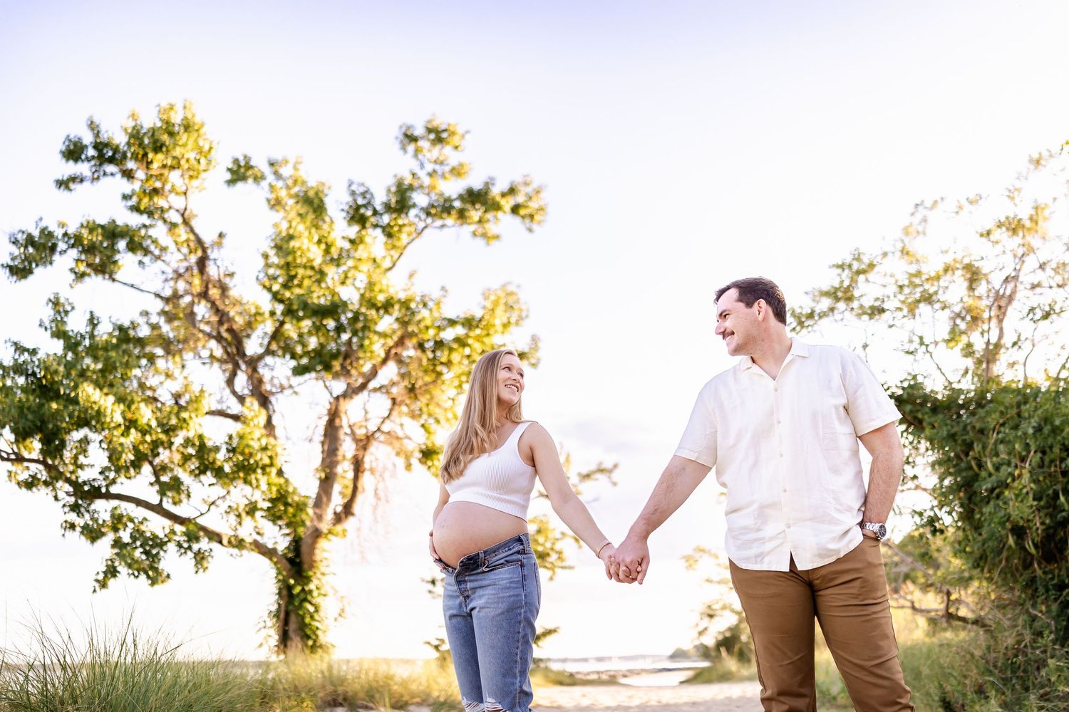 Couple holding hands while walking on path during sunset maternity photo session.