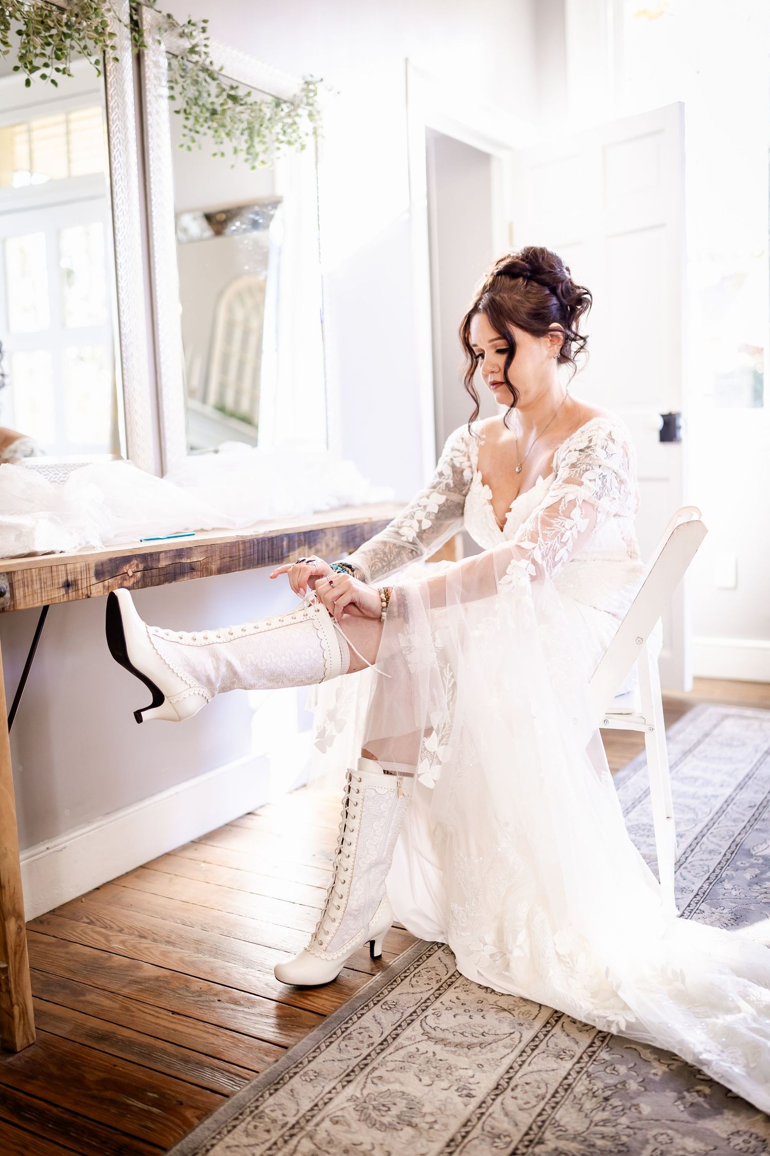 A person in a white wedding dress sits gracefully on an elegant white sofa in a bright, sunlit room.