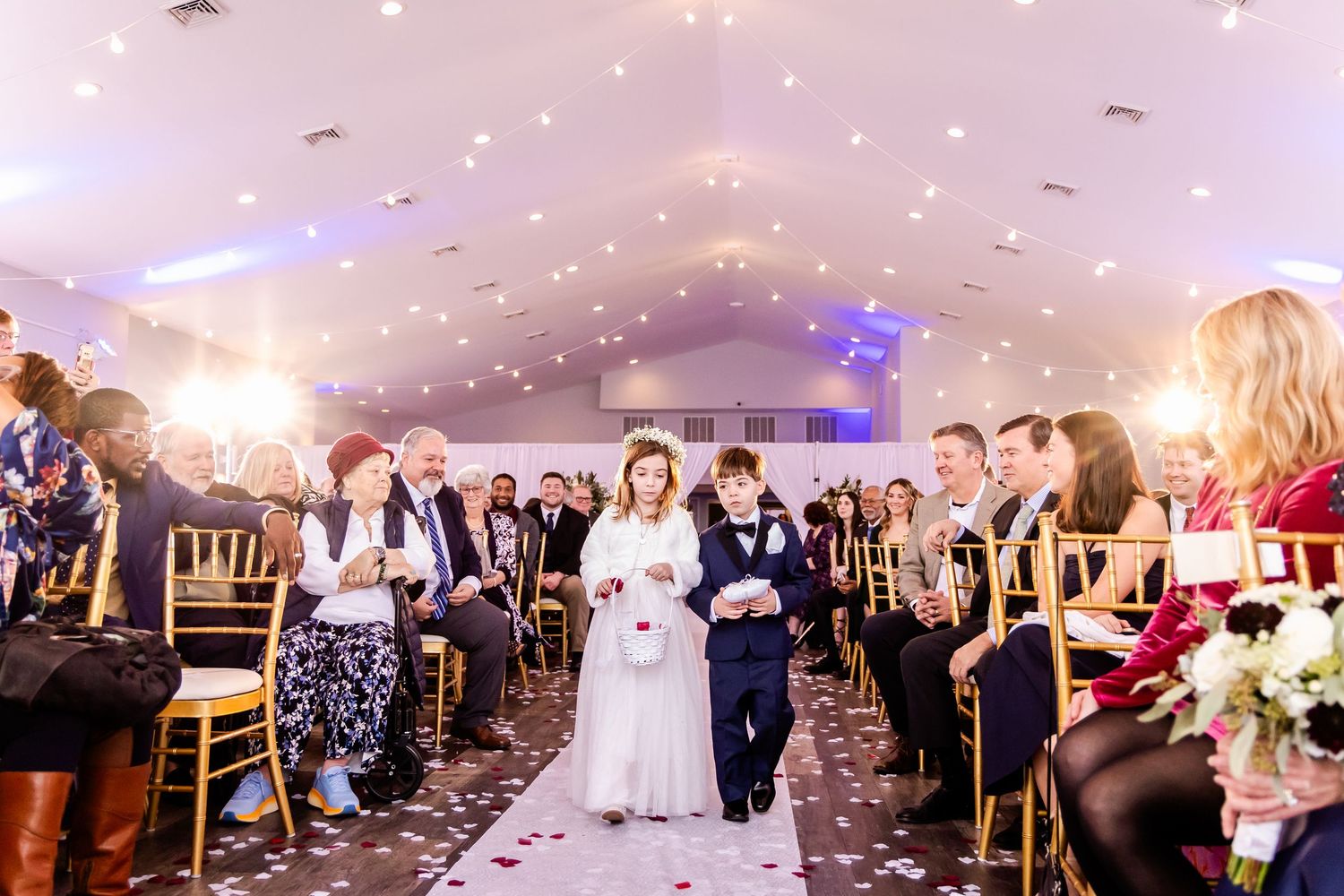 Wedding reception guests dance and celebrate on a dimly lit dance floor with twinkling lights overhead at an elegant venue.
