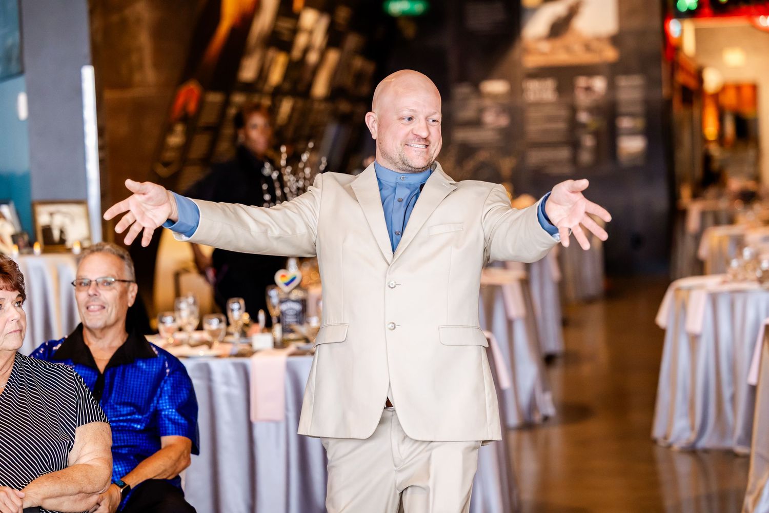 Wedding guests dancing and celebrating on the dance floor at an indoor reception venue with elegant table settings.