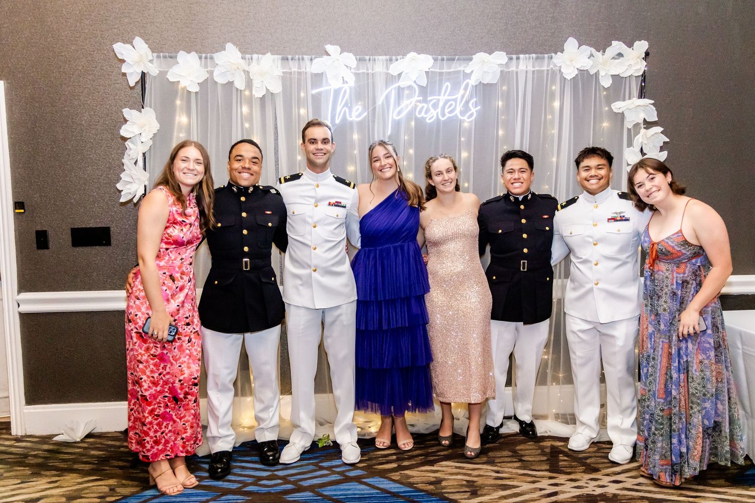 Wedding party group photo with bridesmaids and groomsmen lined up against a gray backdrop.