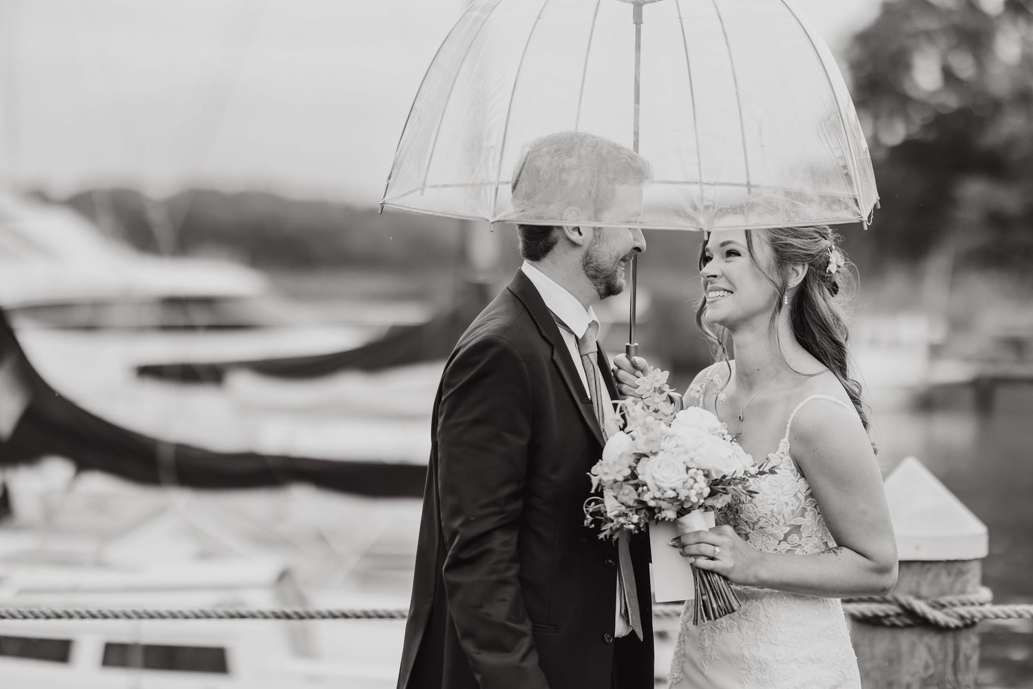 Black and white wedding photos showing couple with umbrella near boats and water.
