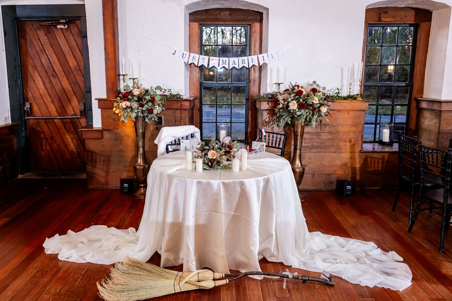 An elegant wedding reception table setup with white linens and floral centerpieces in a rustic wooden venue.