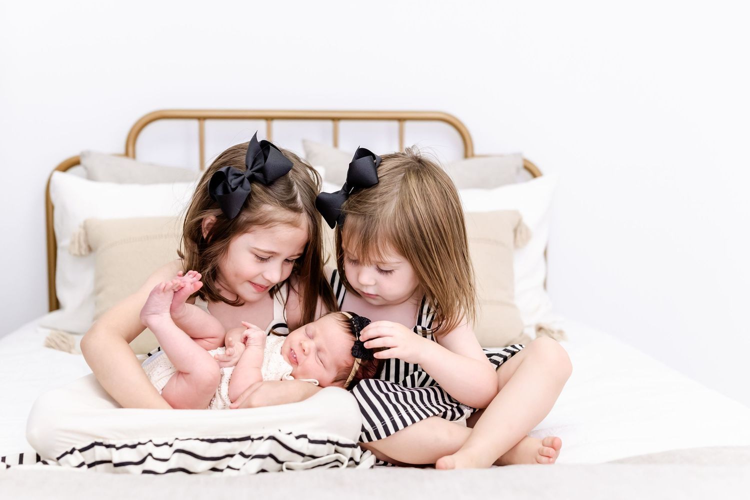 Parents lying on white bed with newborn baby and young child sharing tender family moment together.