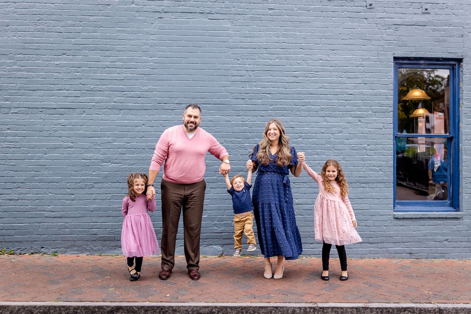 Family posing against a blue painted brick wall on an urban street.