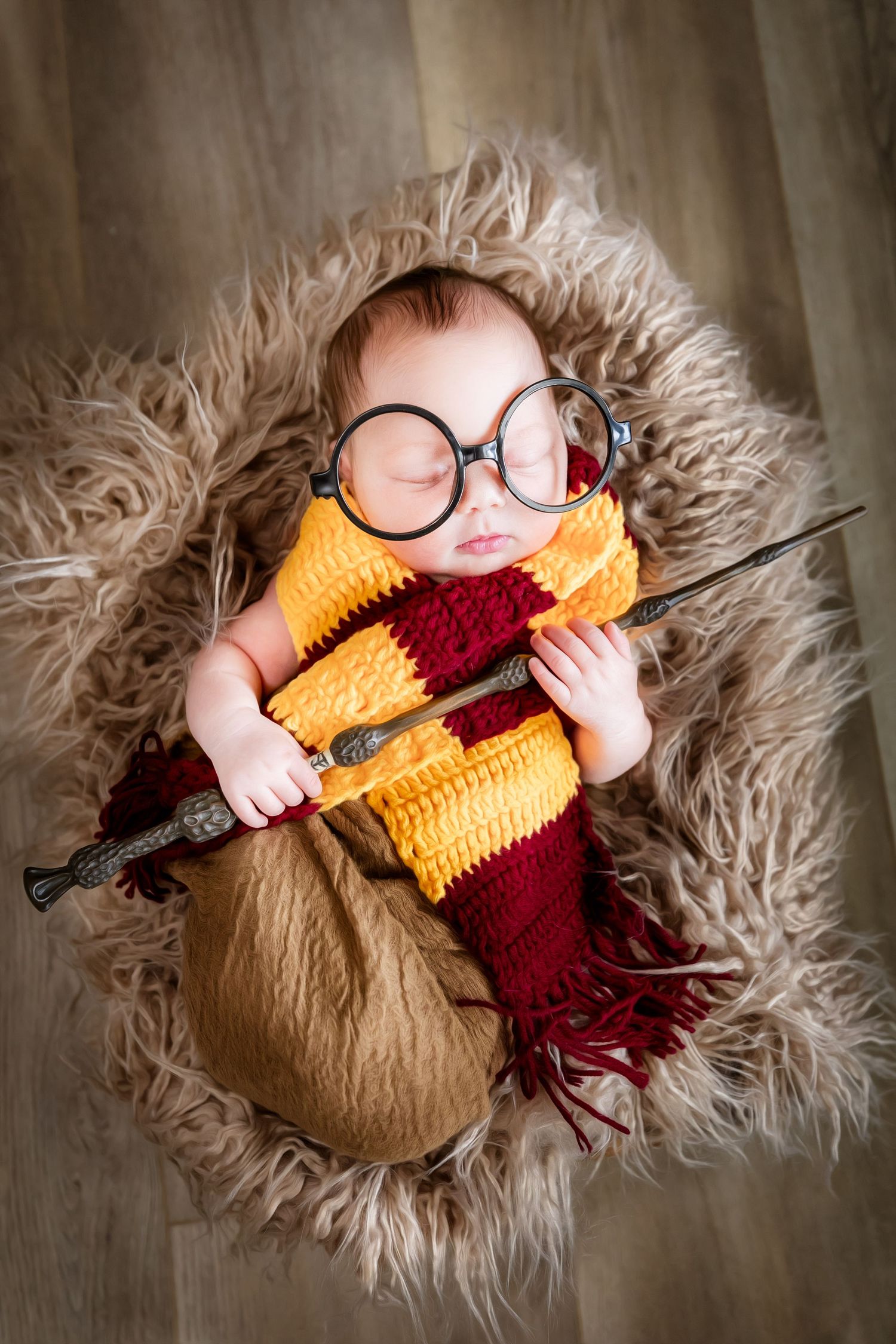 Newborn photography featuring baby in Harry Potter themed outfit with wand on furry backdrop.