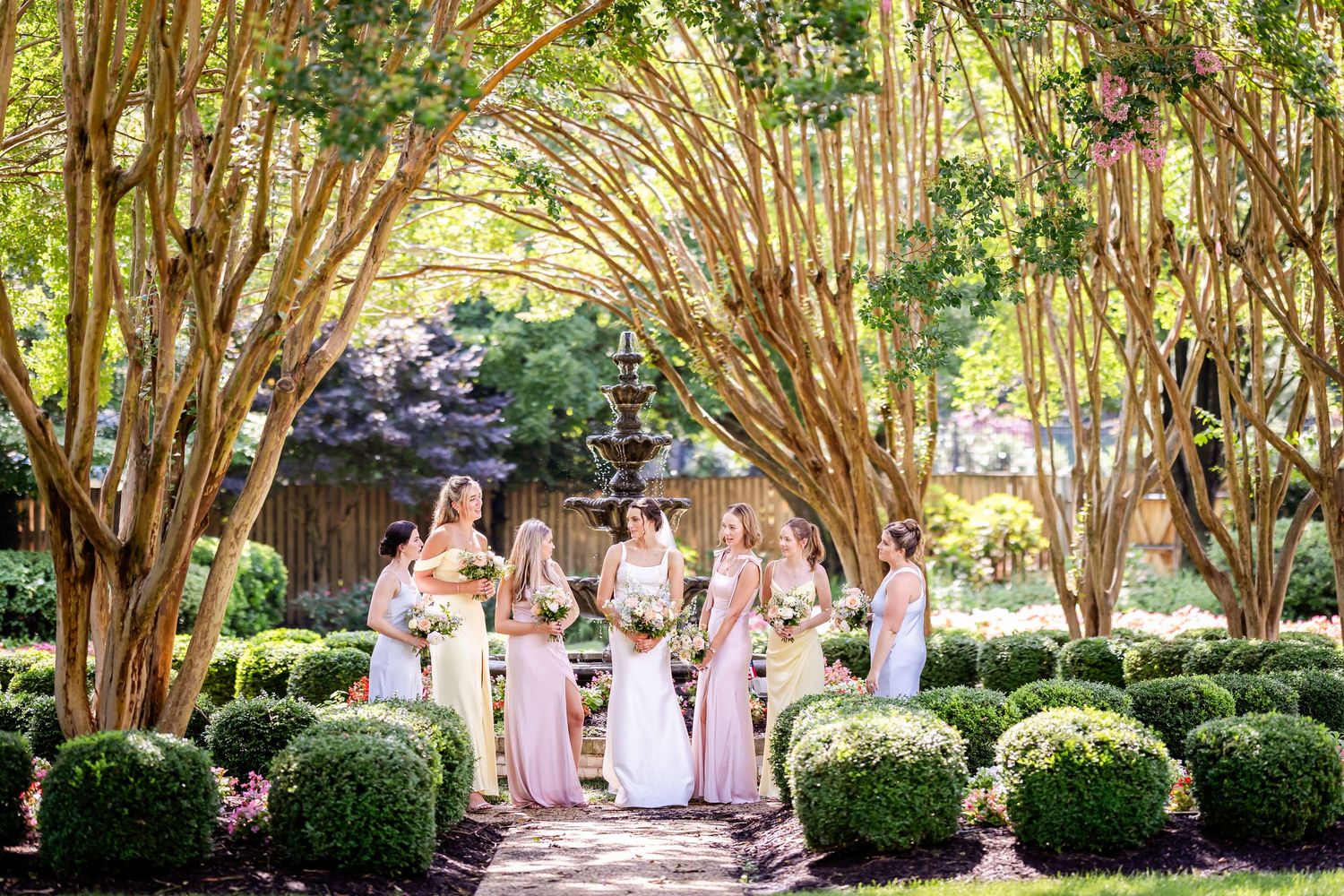 A wedding ceremony takes place under a natural bamboo archway in a lush garden setting.