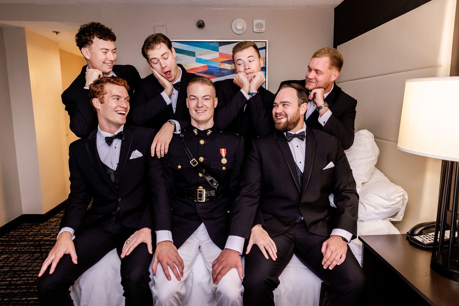 Groomsmen in black tuxedos pose together on a couch for a candid wedding photo.