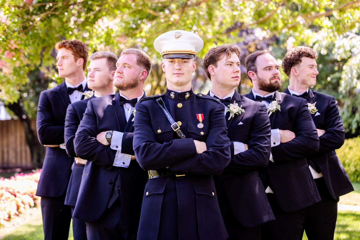 A group of groomsmen in formal navy uniforms pose together outdoors for a wedding photo.