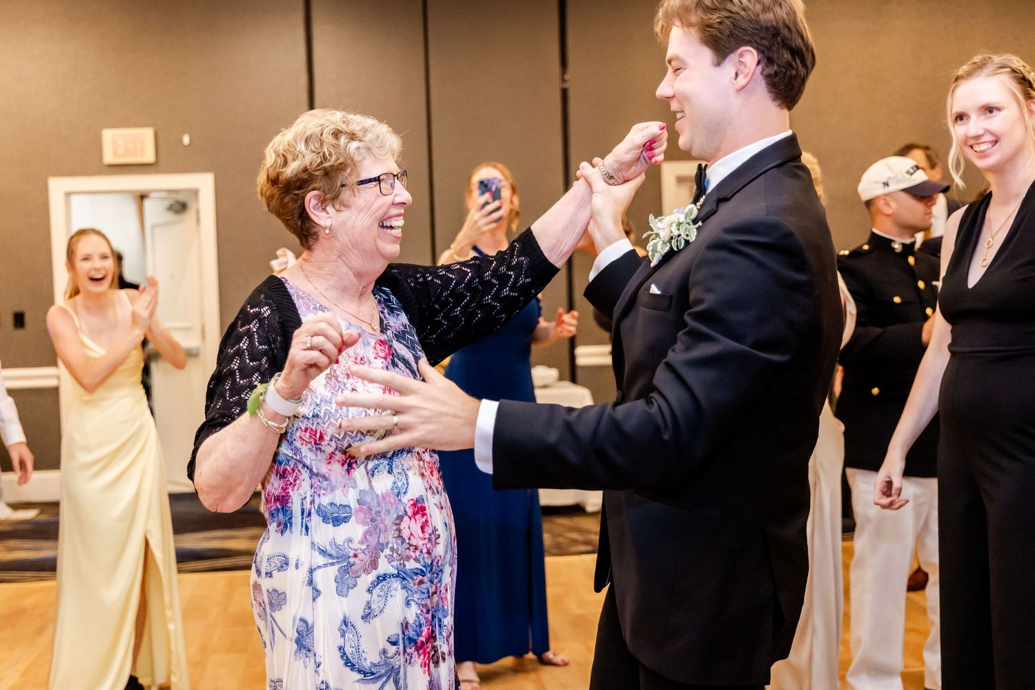 Wedding guests mingling and dancing at a reception with floral centerpieces and warm lighting.