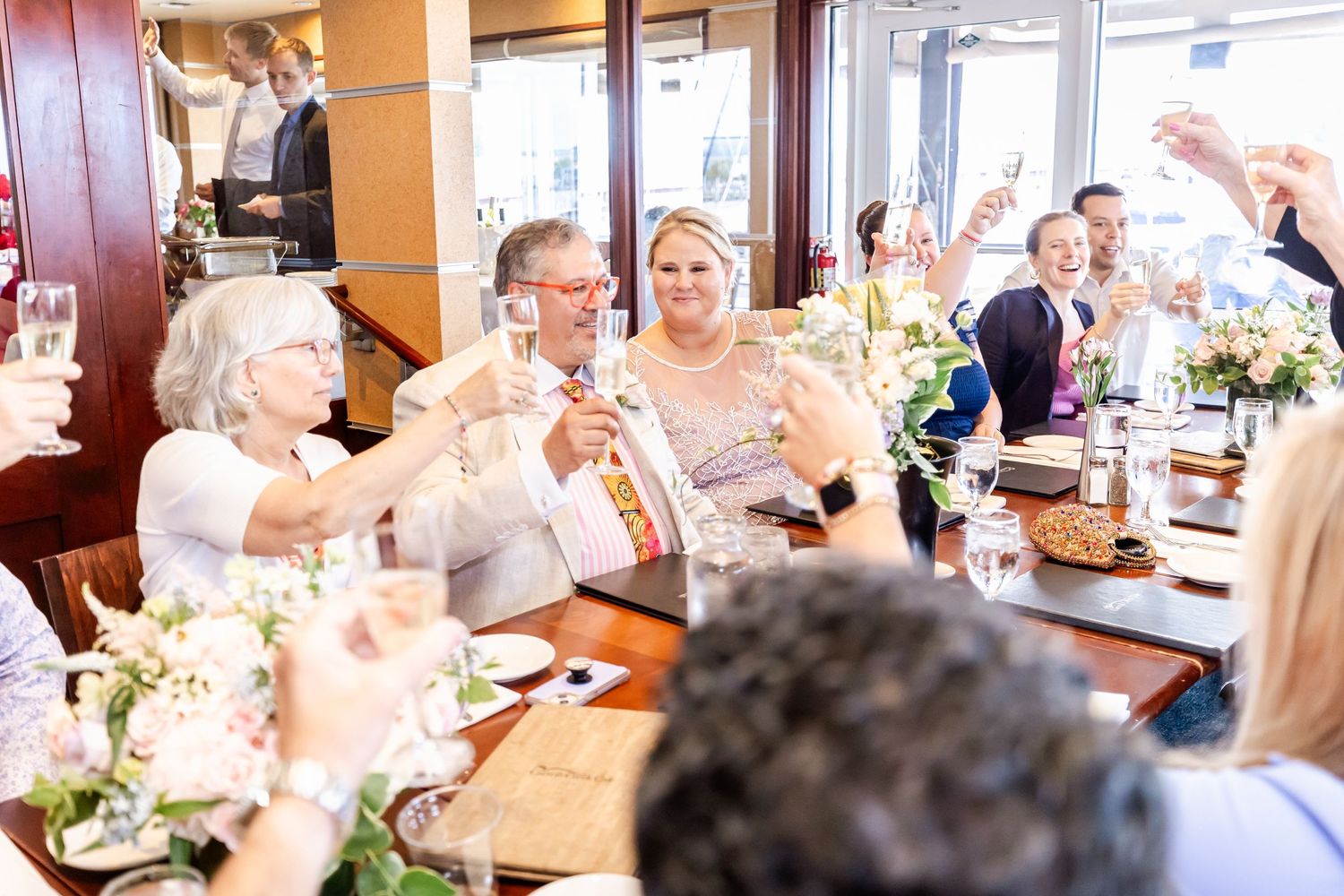 Guests raise glasses in a joyful wedding celebration toast around an elegantly set dining table.