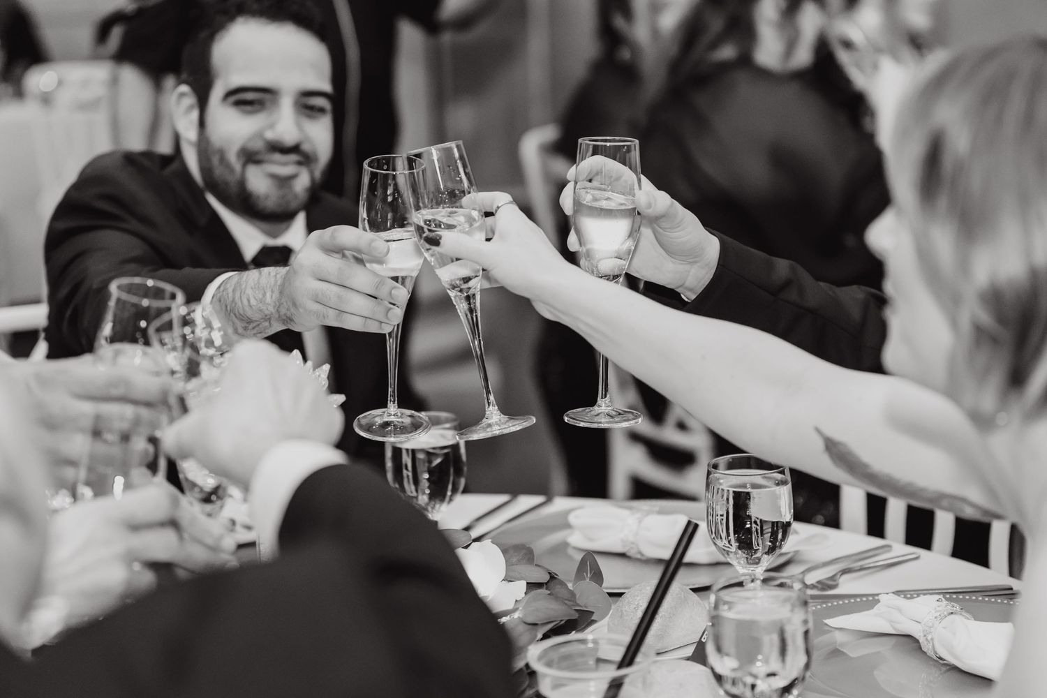 Wedding guests raise champagne glasses for celebratory toast at reception dinner.