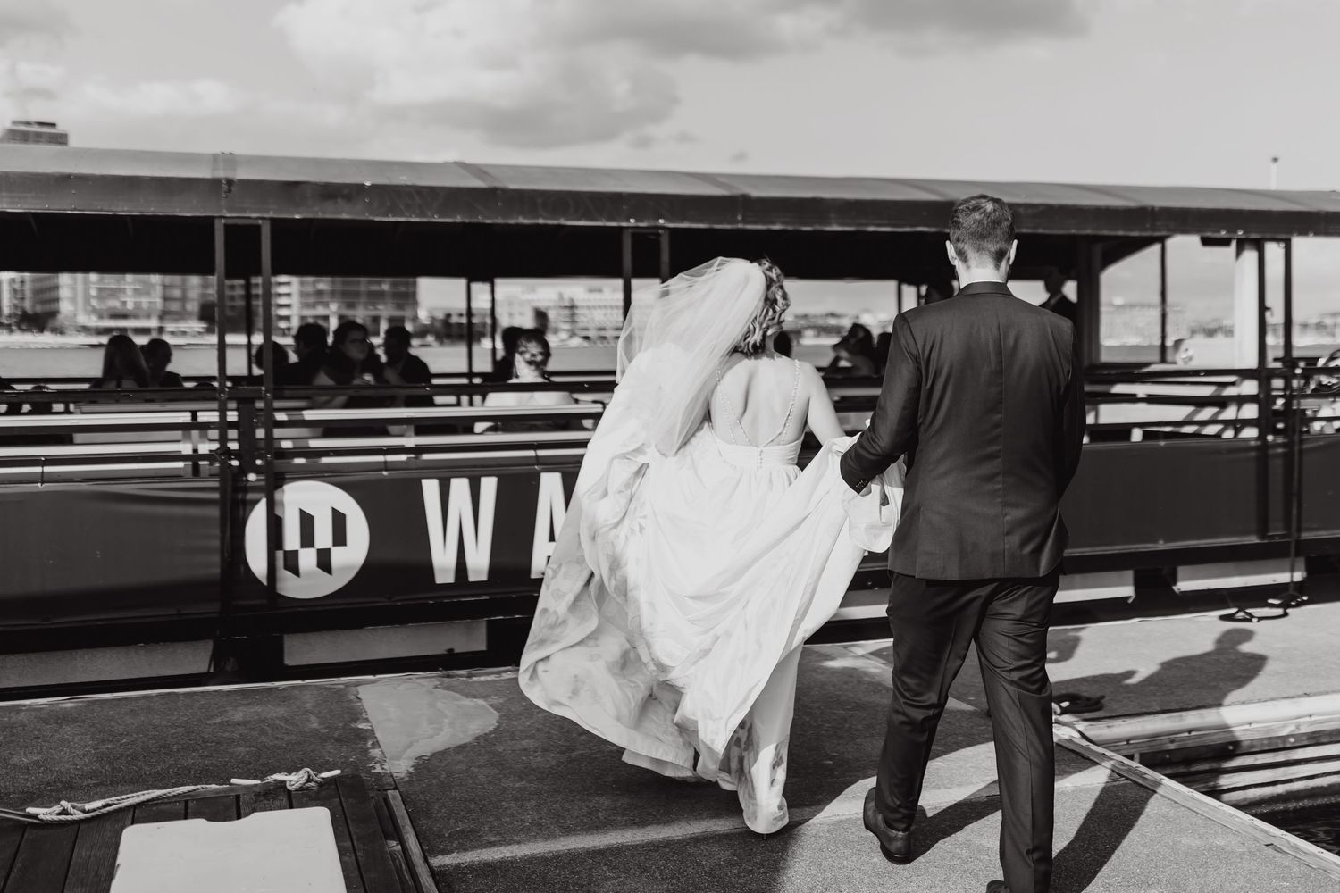 Black and white photo of wedding couple walking on waterfront boardwalk.