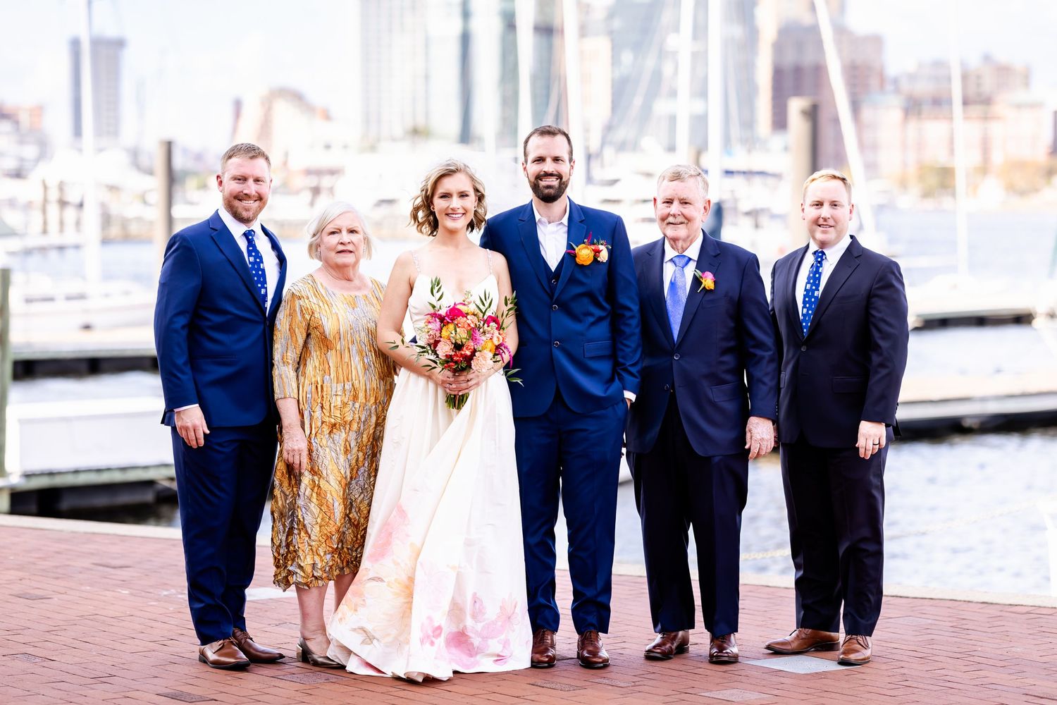 Wedding party poses together on a marina dock with boats and water in the background.