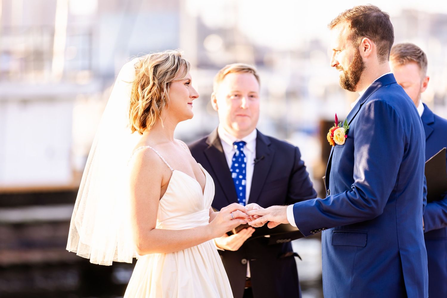 Wedding ceremony exchange of rings on waterfront pier during golden hour.