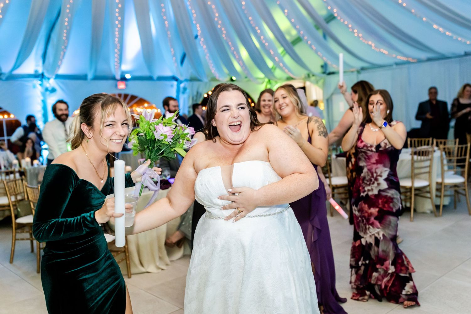 Celebration under blue-lit tent ceiling with joyful dancing at wedding reception.
