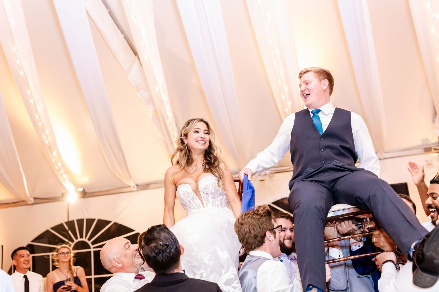 Wedding reception guests celebrate and dance together under an elegant white tent during evening festivities.