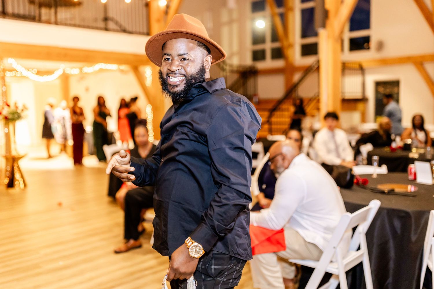 Smiling guest in brown hat and black jacket enjoying the wedding reception.