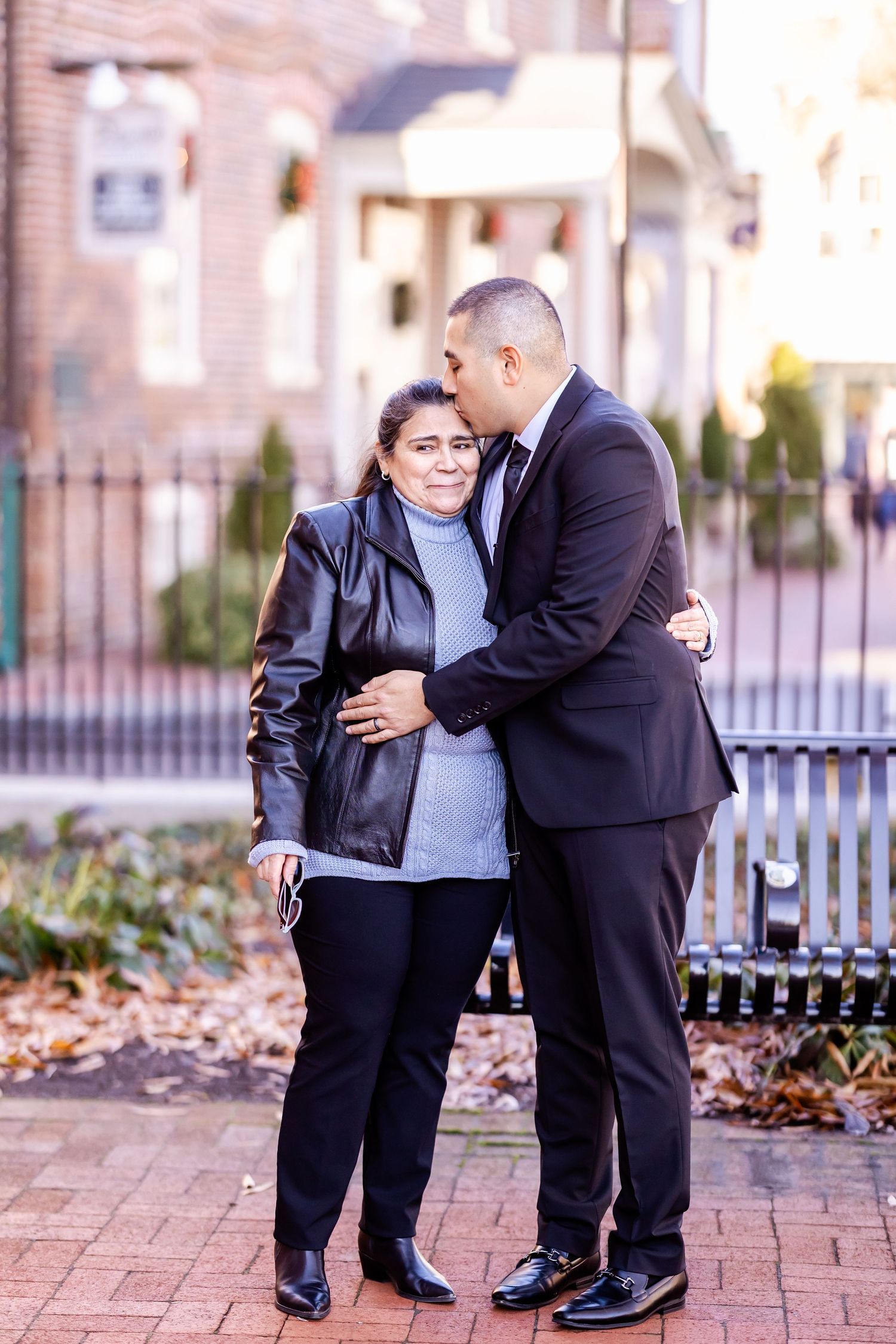 Tender moment between two people in formal attire on brick walkway.