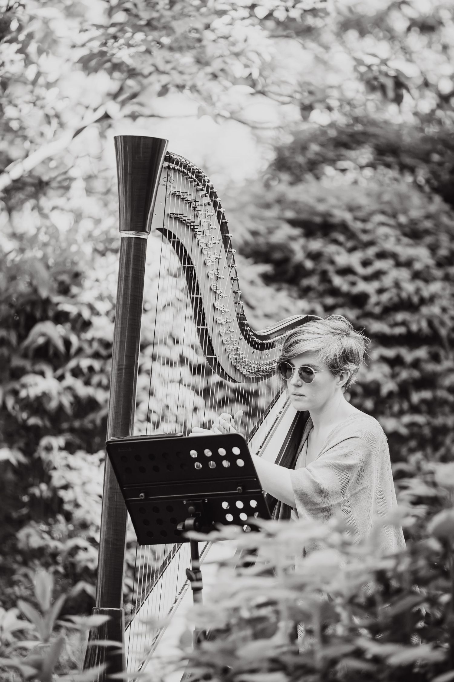 Black and white photograph of harpist performing in garden setting.