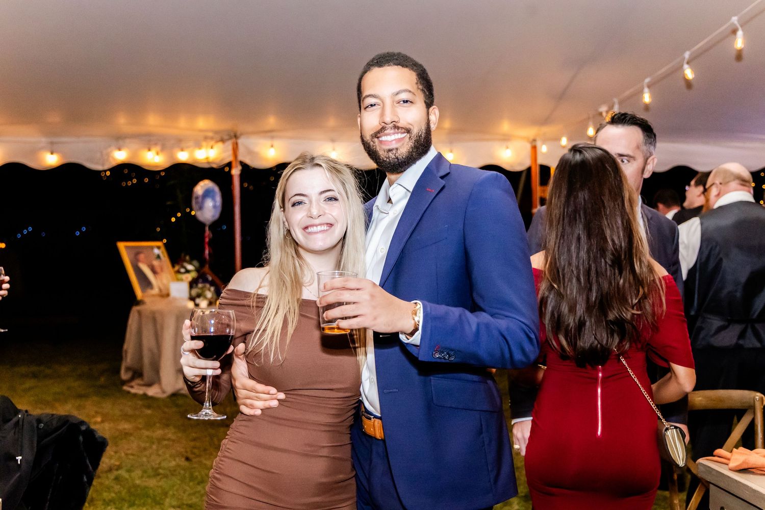 Guests enjoying drinks and conversation at an evening tent reception with string lights.