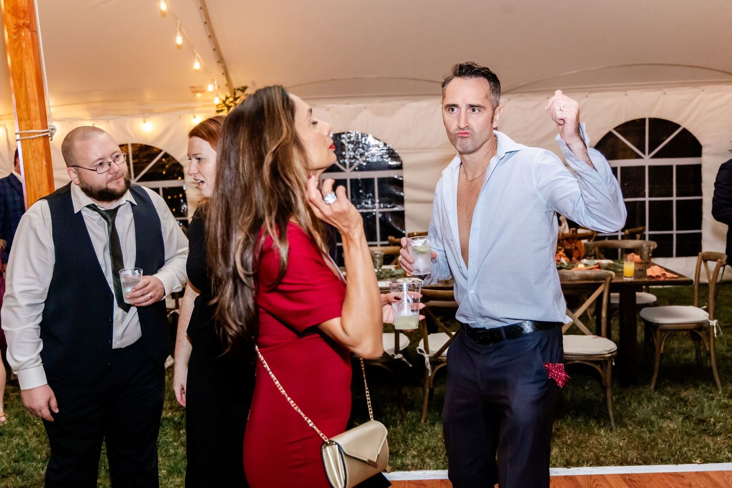 Evening reception party with guests dancing and socializing under a tent with string lights.