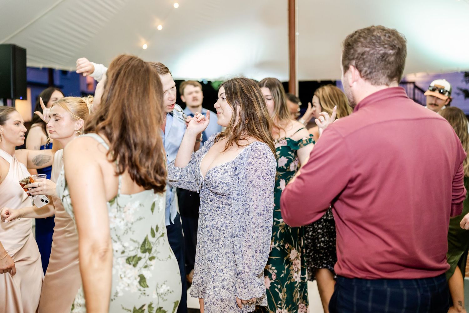 Wedding reception guests dancing and celebrating under tent lighting.