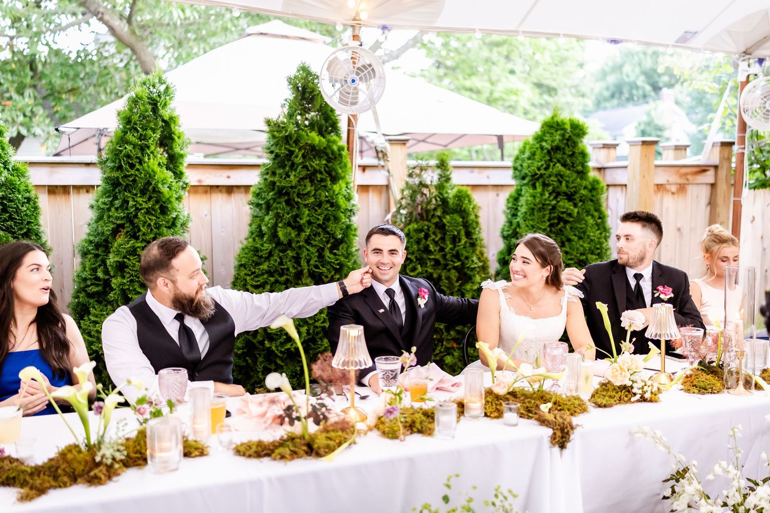 Wedding party seated at an elegantly decorated head table with greenery and candles.