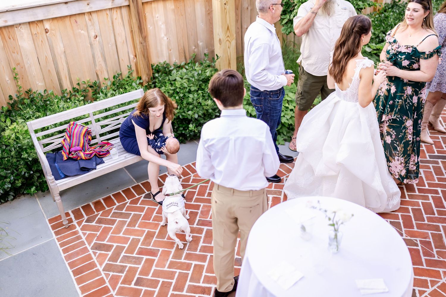 Wedding guests gather on a brick patio during an outdoor reception celebration.