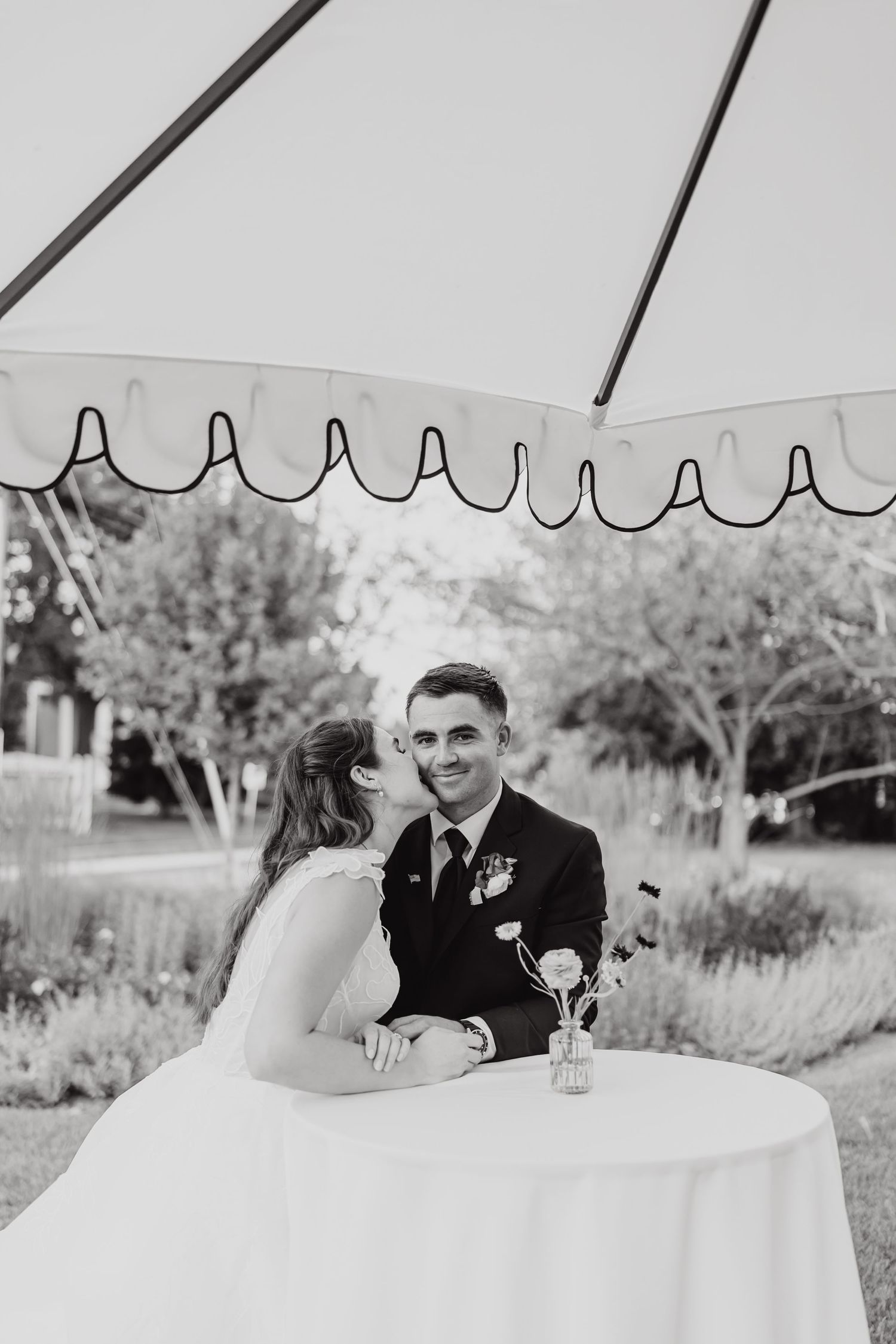 Couple shares an intimate moment under a decorative white umbrella in a garden setting.