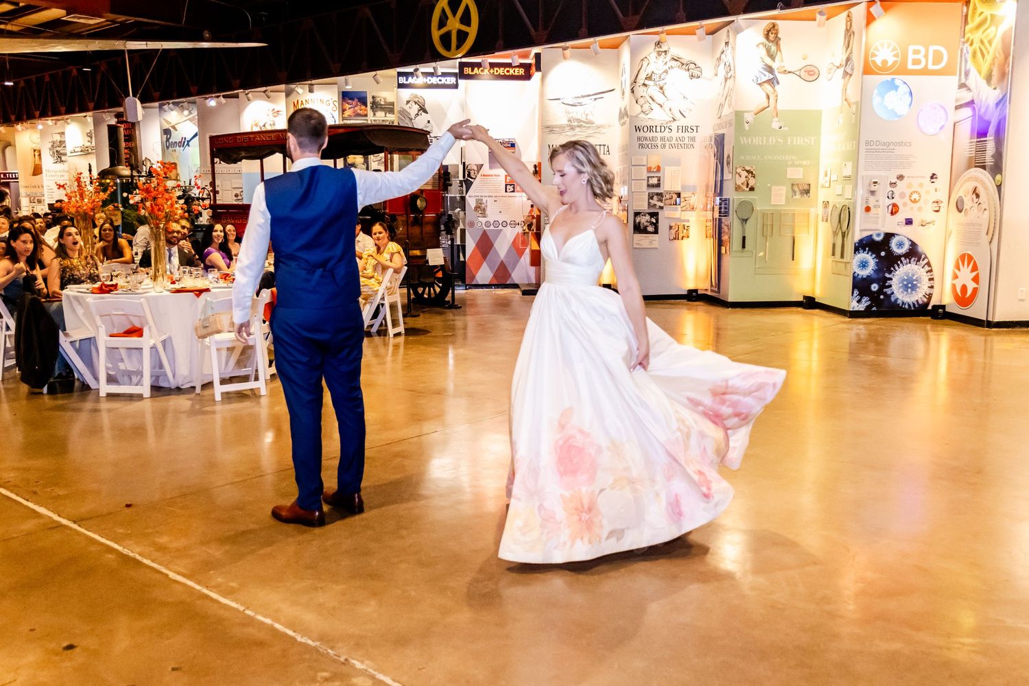 A couple dancing on a polished floor in an event space with white chairs and tables in the background.