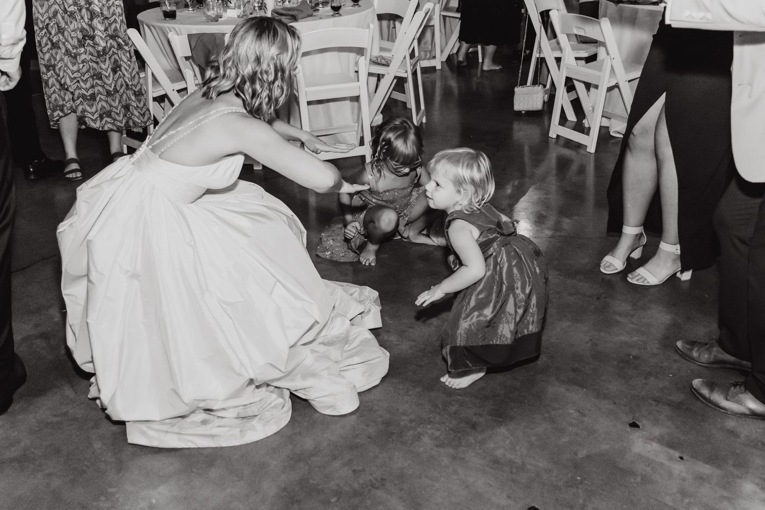 Black and white photo of wedding guest kneeling to interact with small child at reception.
