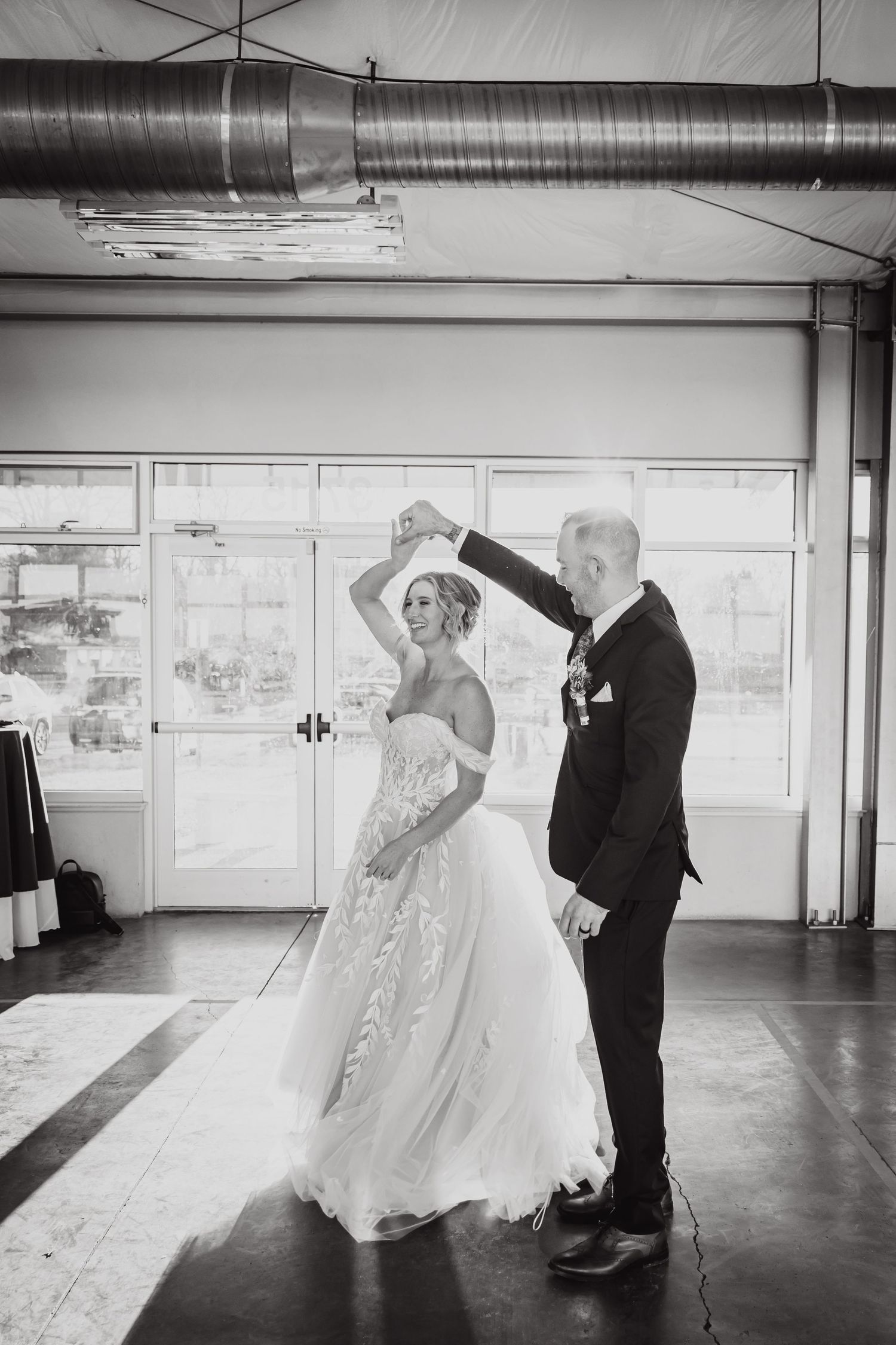 A couple dances in an industrial venue with exposed ductwork during their wedding celebration.