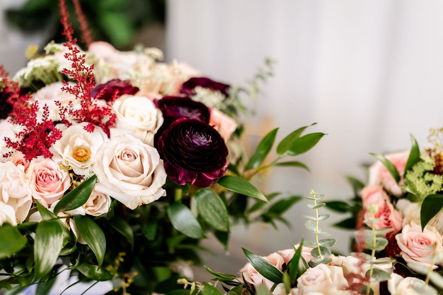 Wedding bouquet features blush pink roses and deep burgundy flowers with lush greenery.
