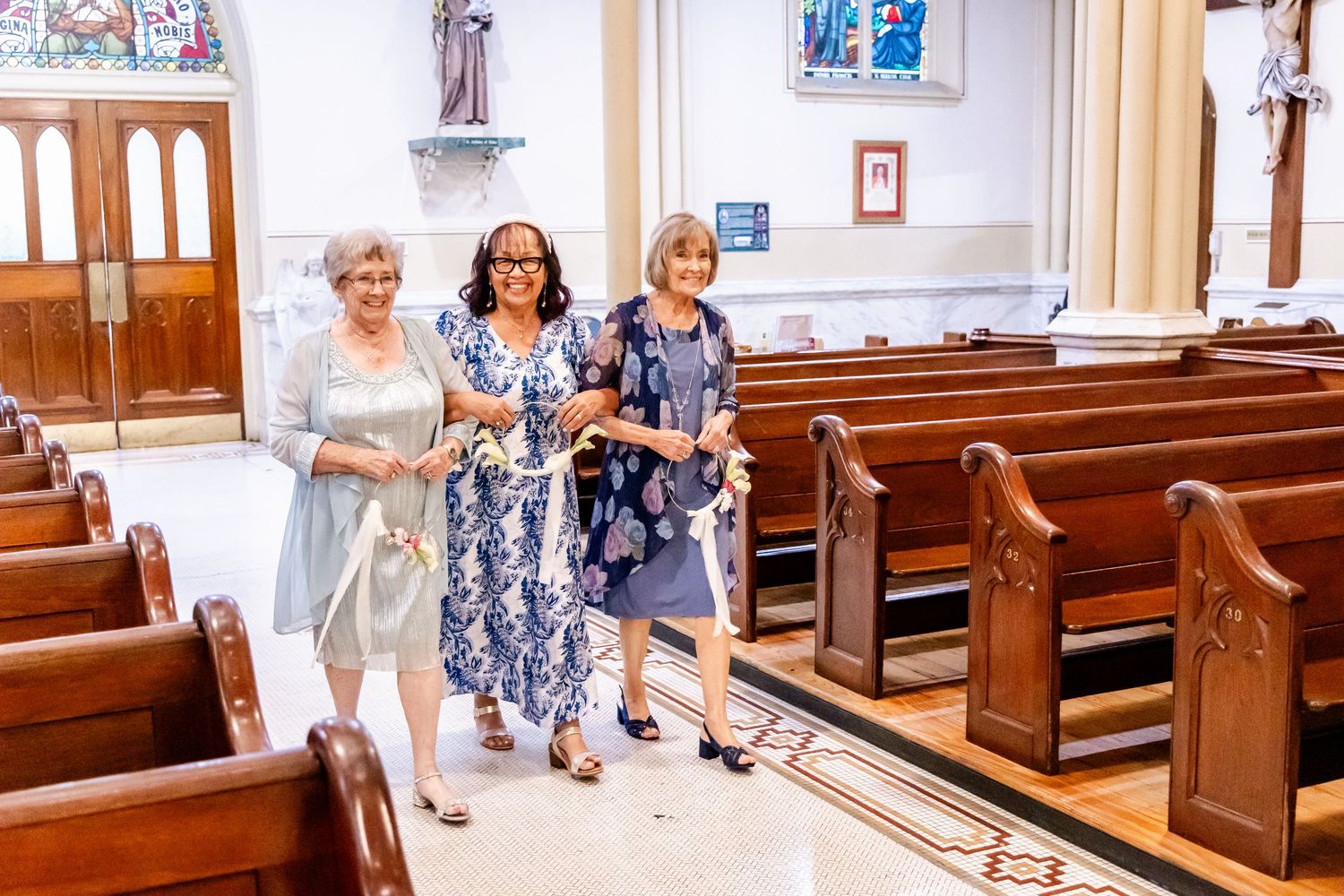Wedding guests walking through the aisle of a traditional church with white walls and wooden pews.