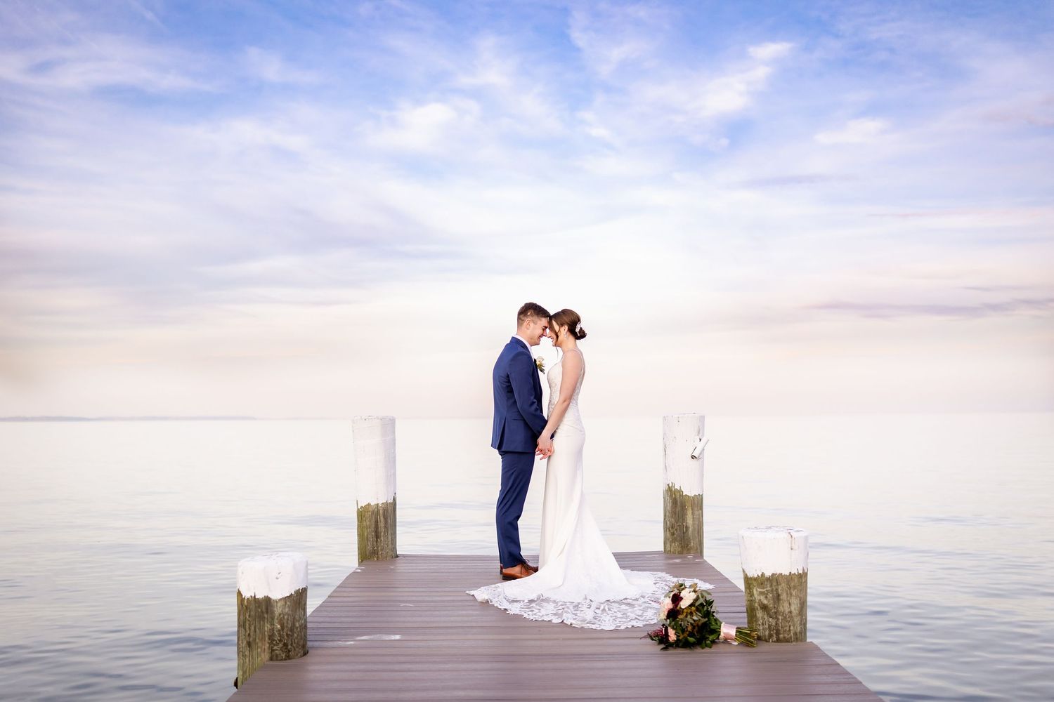 Couple shares intimate moment on wooden pier during waterfront wedding photoshoot.