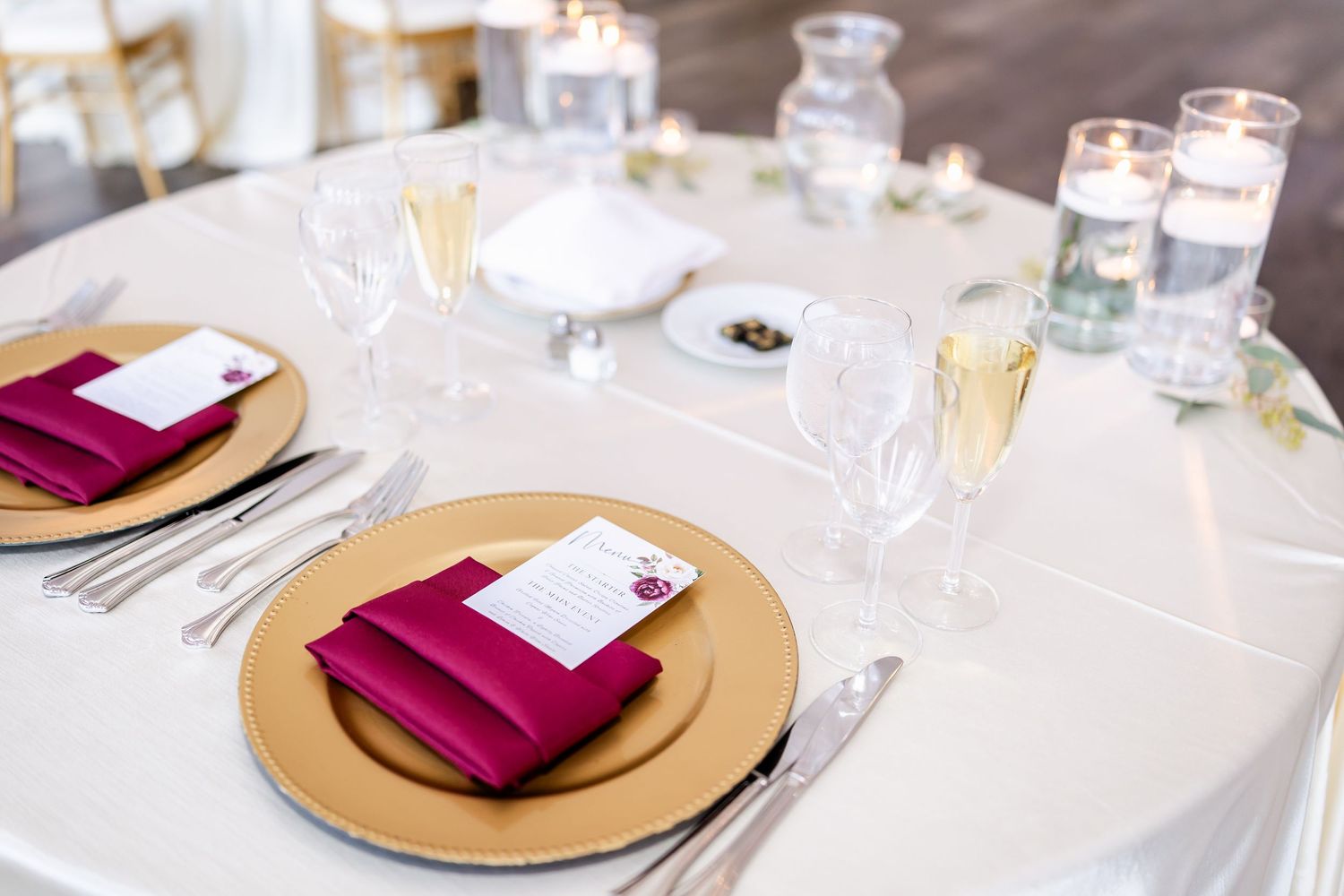 Elegant wedding reception table settings with burgundy napkins and gold charger plates.
