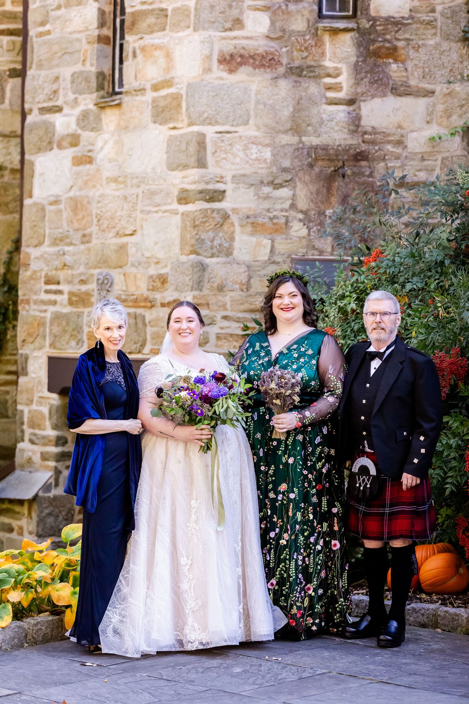 Wedding party portrait featuring traditional Scottish dress outside a stone church building.
