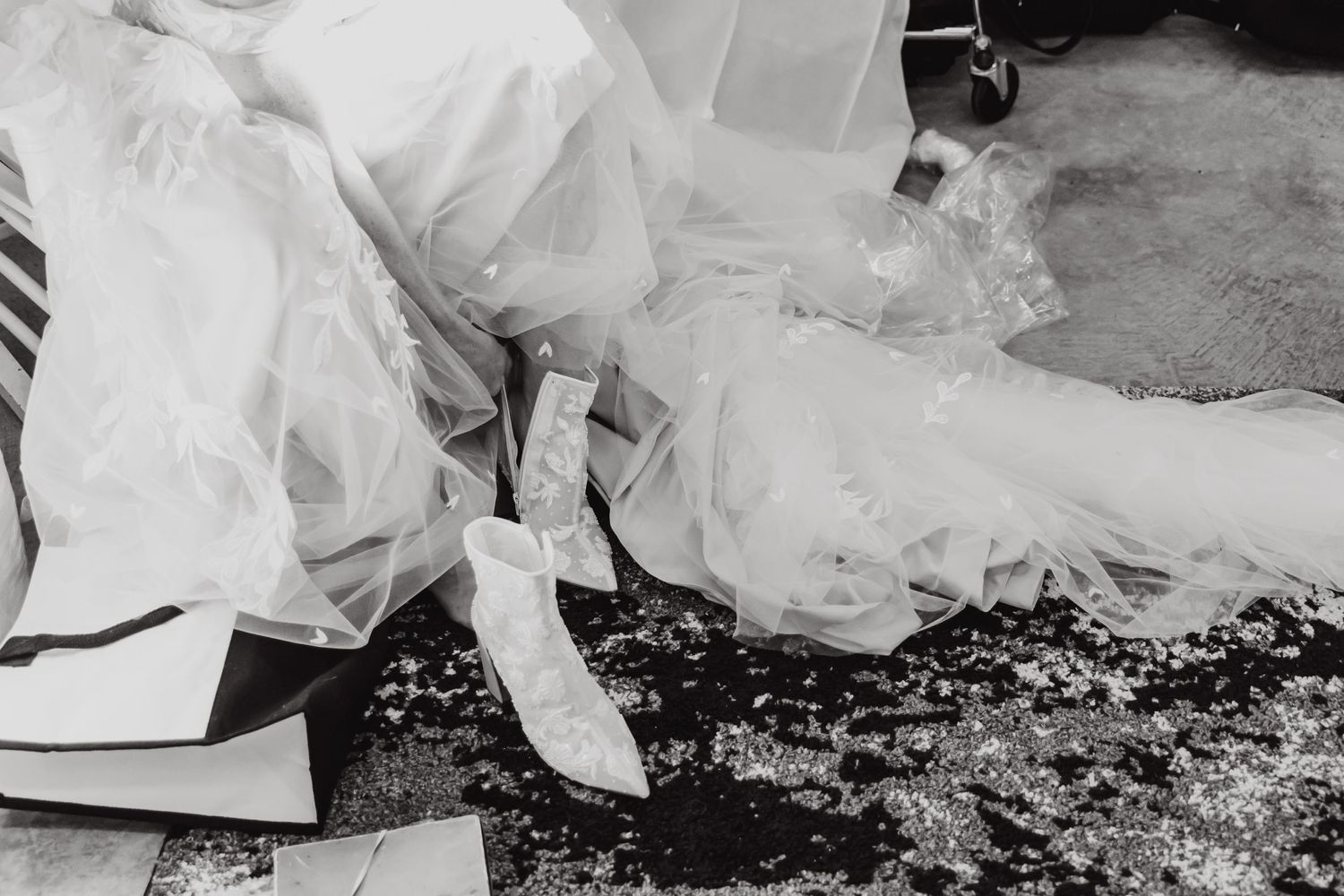 A black and white detail shot of a bride's wedding dress and shoes against a textured ground.