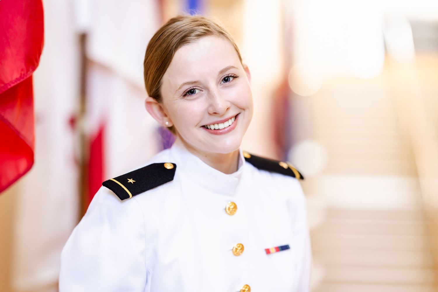A Navy officer in dress whites with gold buttons and insignia smiles in formal portrait.