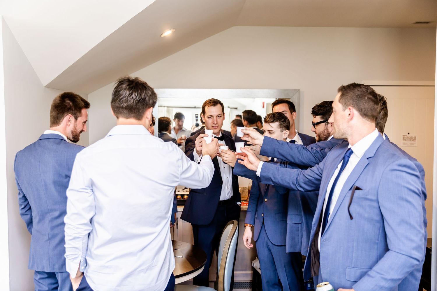 Groomsmen help adjust ties and jackets while getting ready in indoor venue.
