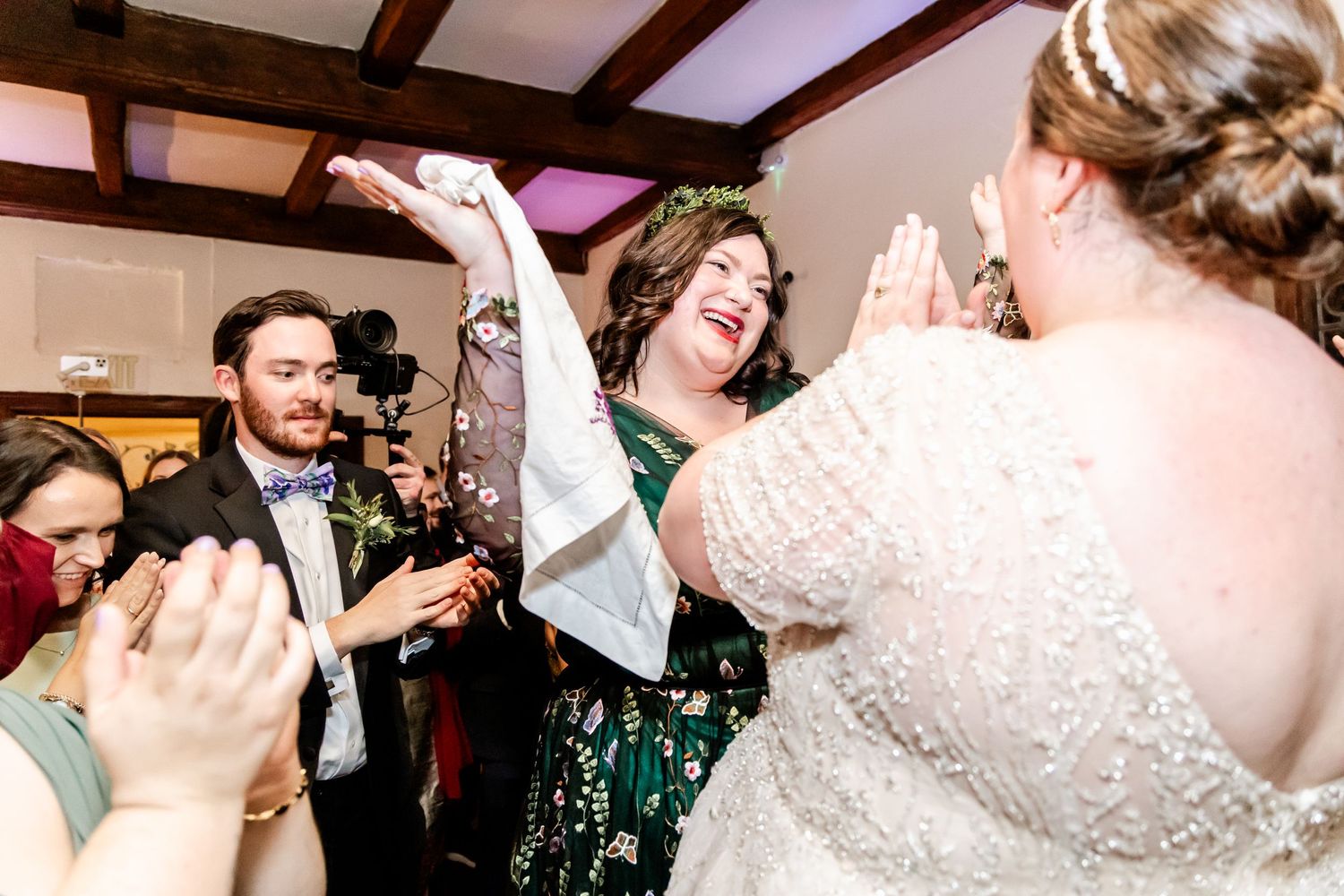 Reception celebration with guests dancing and cheering in a rustic venue with wooden beams.