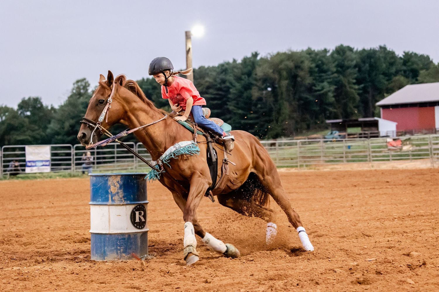 Horse and rider perform a tight turn around a blue barrel during a rodeo competition.