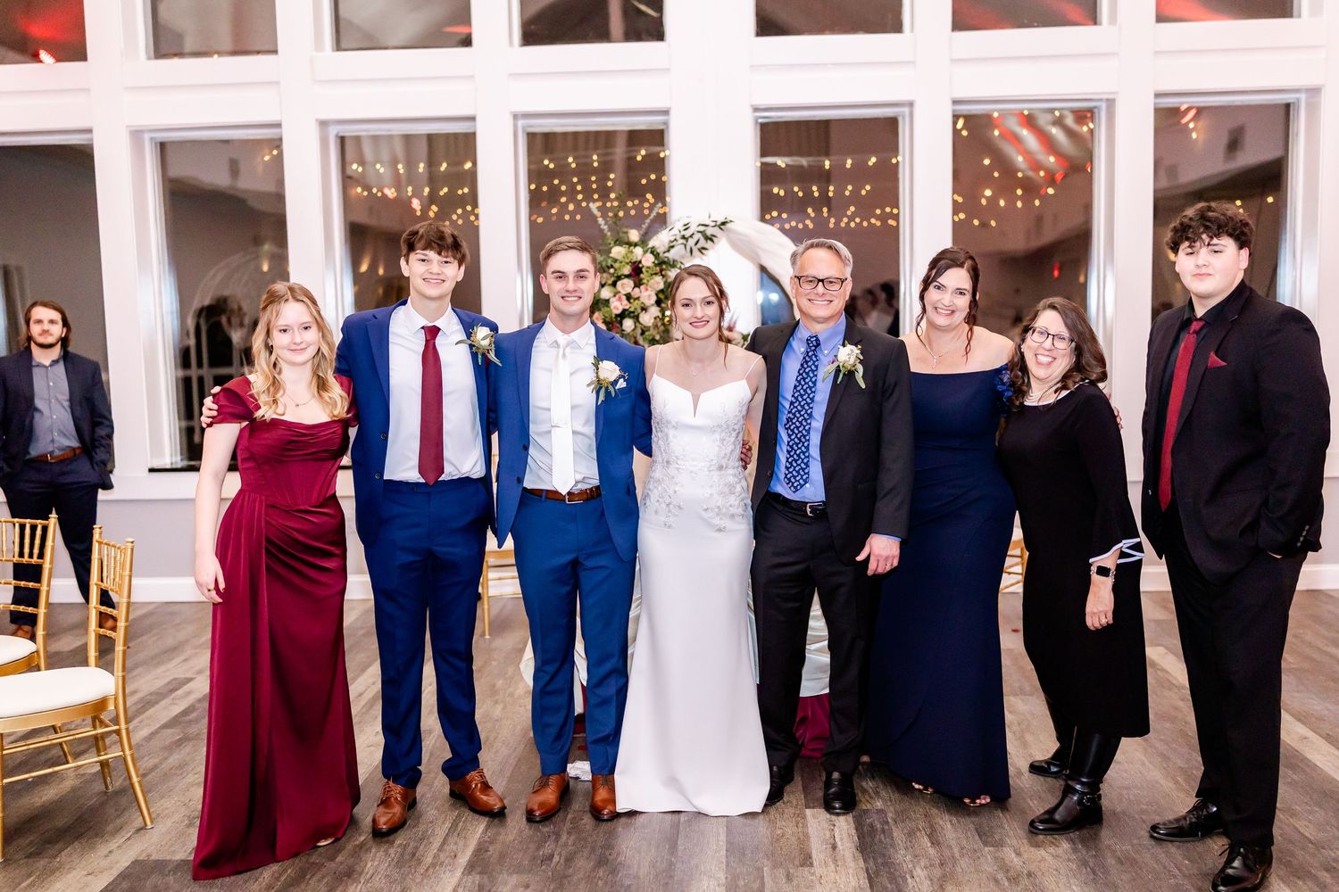 Large group wedding photo showing guests lined up against white pillars in formal attire.